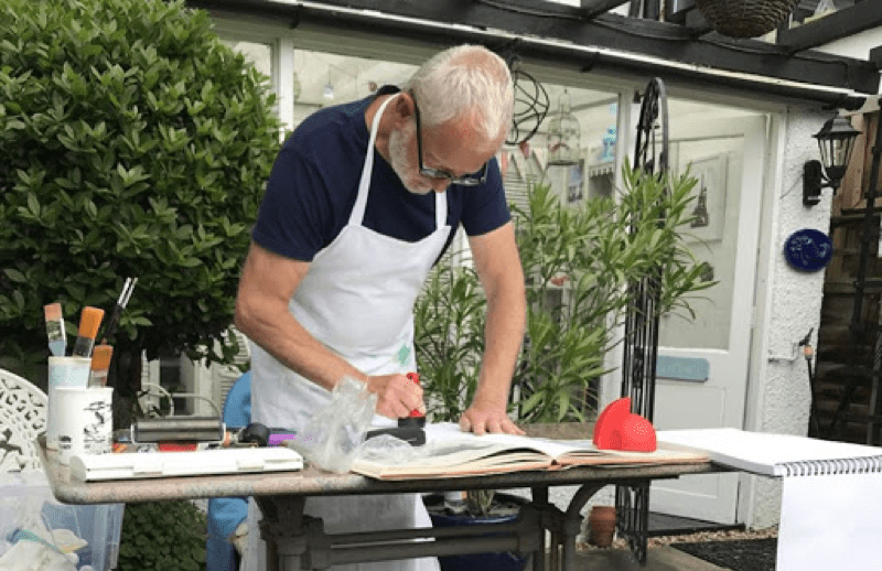 Keith Tunnicliffe, lino printng artist, creating a lino print on a table outside