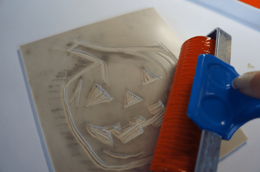 Roller with orange ink being carved onto SoftCut with a pumpkin design