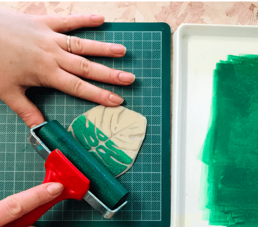 roller being used to apply green block printing ink to carved monstera leaf