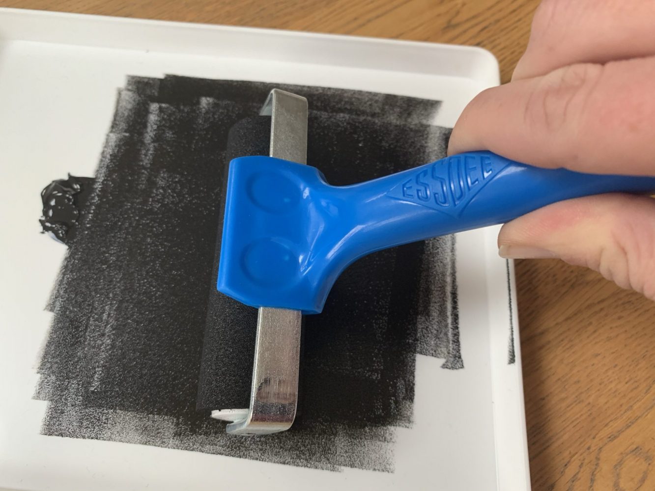 Black fabric ink being rolled out in a white ink tray using a fabric roller