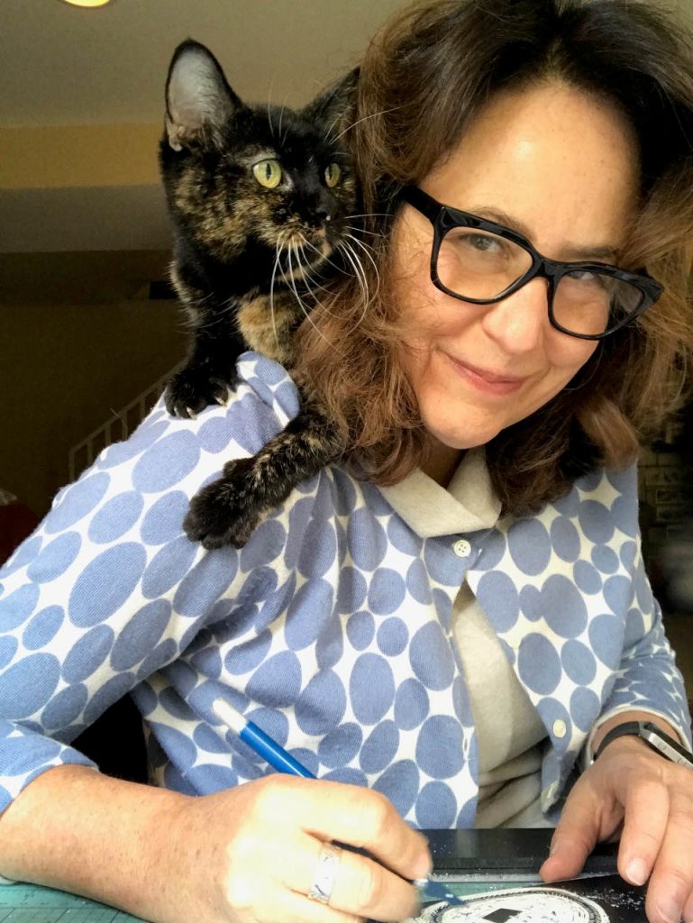 Photo of scraperboard artist Claudia McGehee sat at her desk with her tabby cat