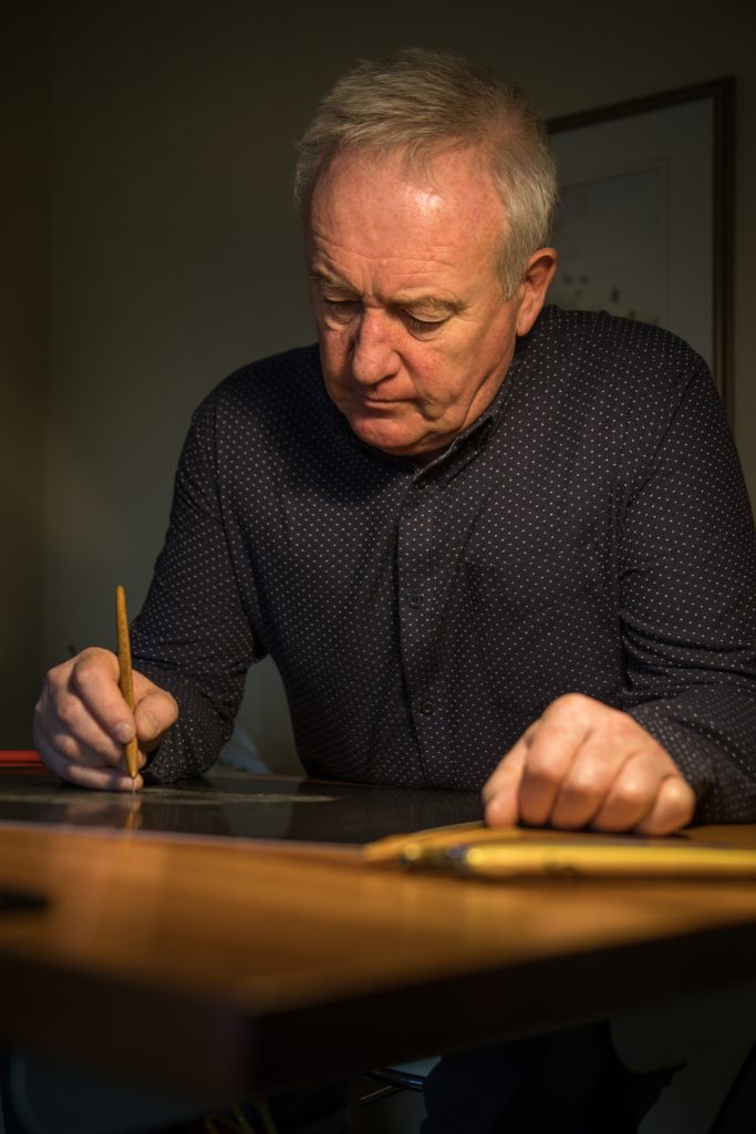 Photo of scraperboard artist Keith Sykes working at a table