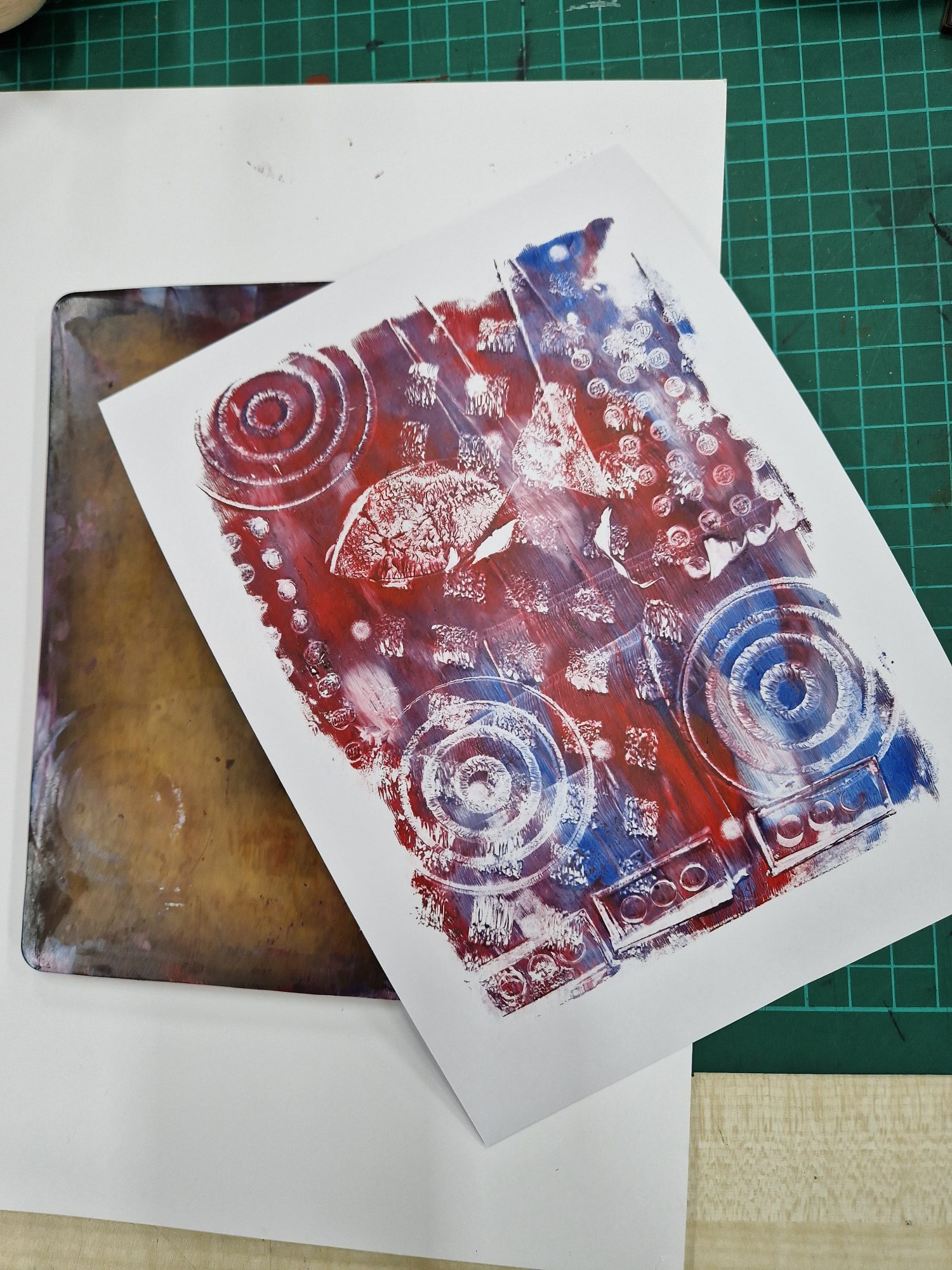 Gelli plate print of blue and red swirls with plate in background